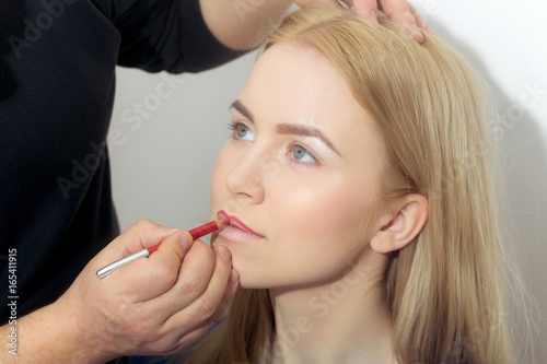 Hand of visagiste applying red pencil on woman lips