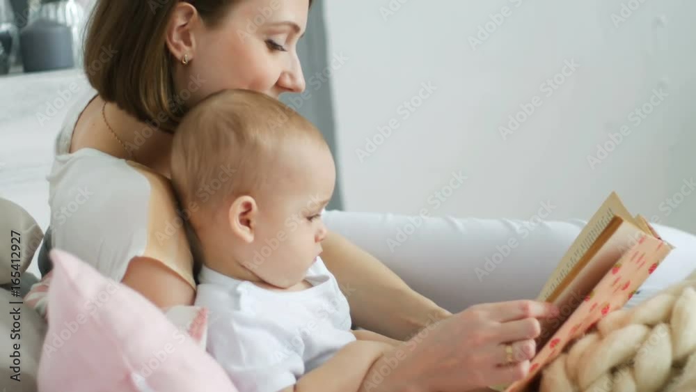Mother and her two years old baby boy are reading book in sunny room Mother and her two years old baby boy are reading book in sunny room