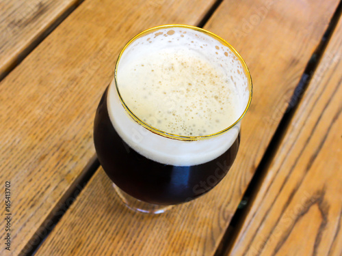 Glass of dark black beer in a round glass on wooden table background