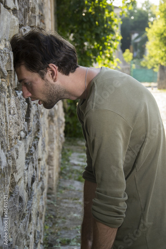 Side view of depressed man leaning his head against a wall