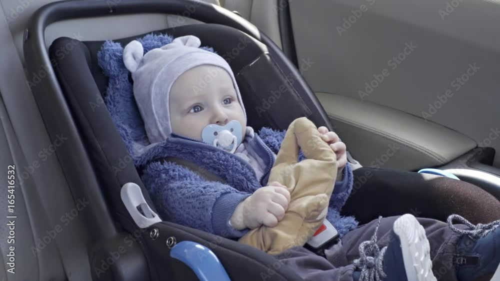 Adorable baby boy lying in car seat with soother in his mouth and playing with bunny toy while riding in backseat of car Adorable baby boy lying in car seat with soother in his mouth and playing with bunny toy while riding in backseat of car
