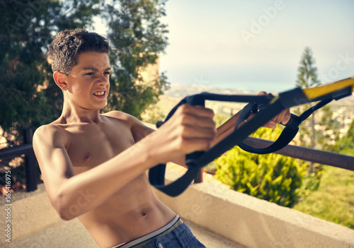 The teenager performs exercises on the TRX simulator. photo