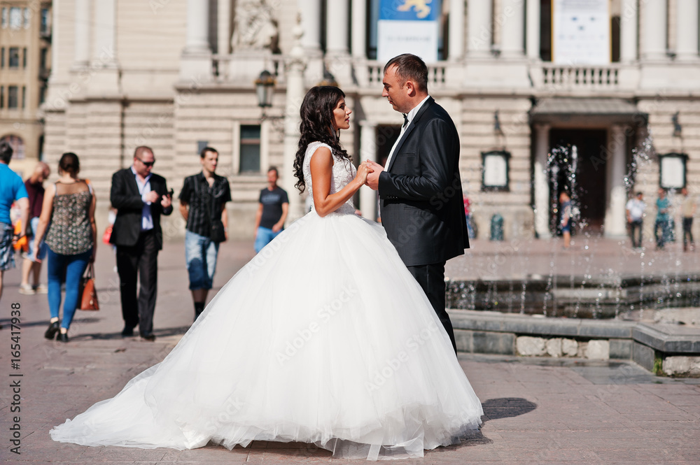 Amazing young attractive newly married couple walking and posing in the downtown with beautiful and ancient architecture on the background on their wedding day.
