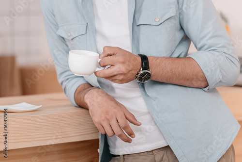 close-up partial view of young man holding white cup and drinking coffee