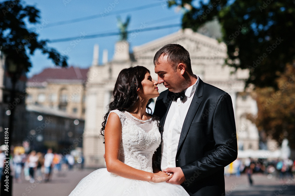 Amazing young attractive newly married couple walking and posing in the downtown with beautiful and ancient architecture on the background on their wedding day. Amazing young attractive newly married couple walking and posing in the downtown with beautiful and ancient architecture on the background on their wedding day.