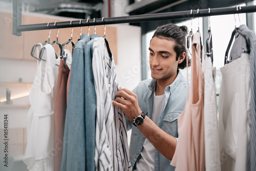 handsome smiling young man working with clothes in boutique