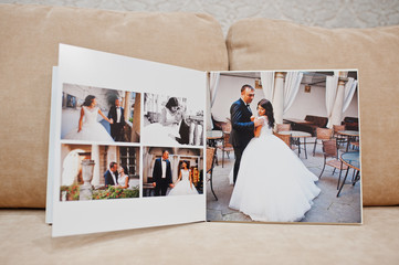 Pages of wedding photobook or wedding album on the sofa with cushions on the background.