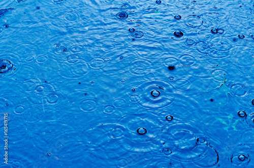 Rain drops on the surface of a street road on a rainy day, toned blue