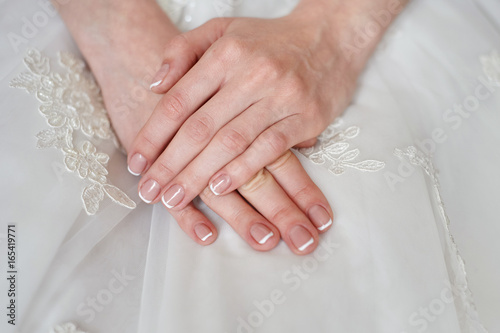 Hands of the bride with a manicure on a white dress background