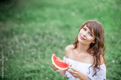 Young beautiful woman sitting on the grass and eat watermelon. Happy girl resting on the grass. Warm summers. Watermelon.