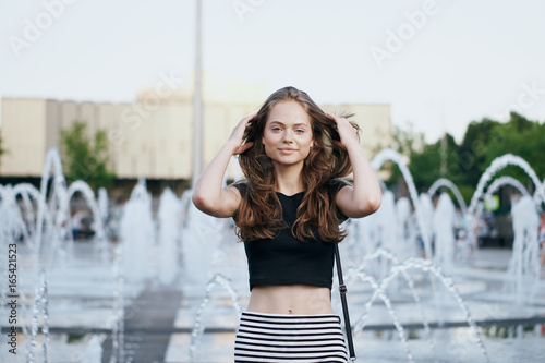 Young beautiful woman is walking along the street in the city in summer