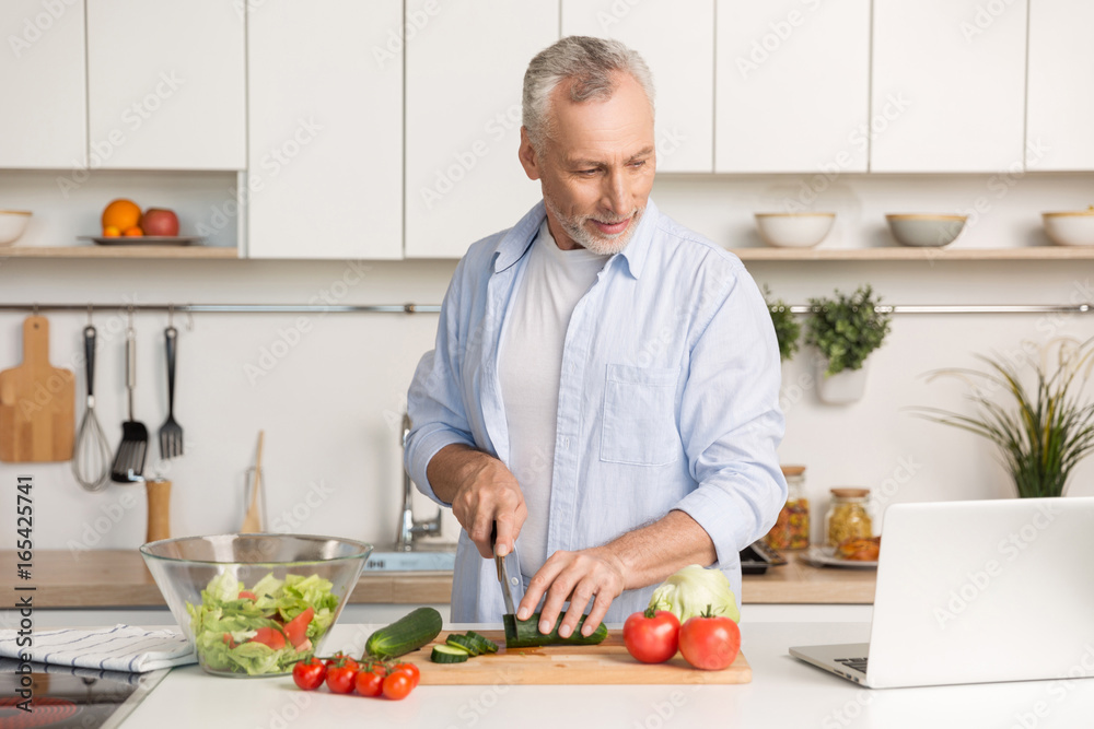 Handsome man standing at the kitchen using laptop and cooking Handsome man standing at the kitchen using laptop and cooking