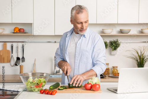 Handsome man standing at the kitchen using laptop and cooking