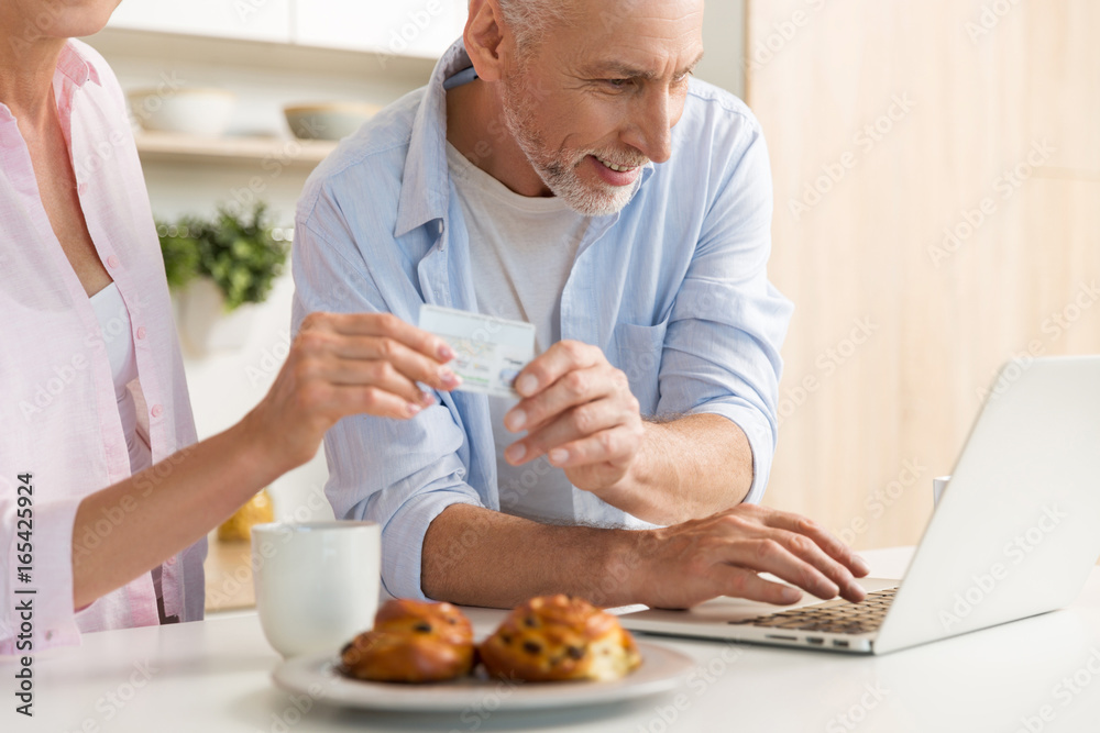 Happy mature loving couple family using laptop holding credit card Happy mature loving couple family using laptop holding credit card