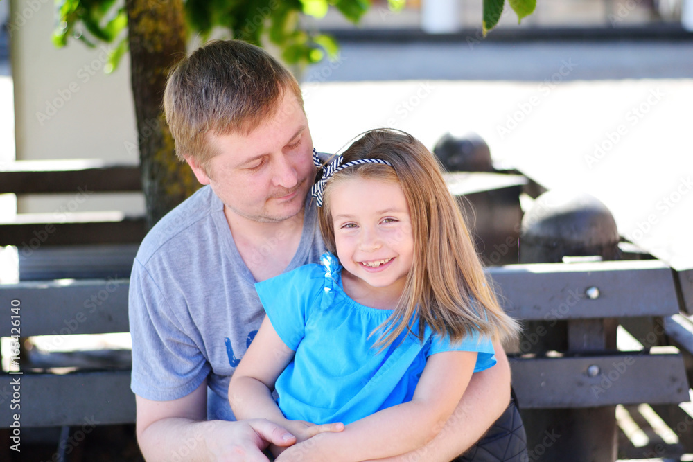 Father hugging daughter on the bench in the park on sunny summer day Father hugging daughter on the bench in the park on sunny summer day