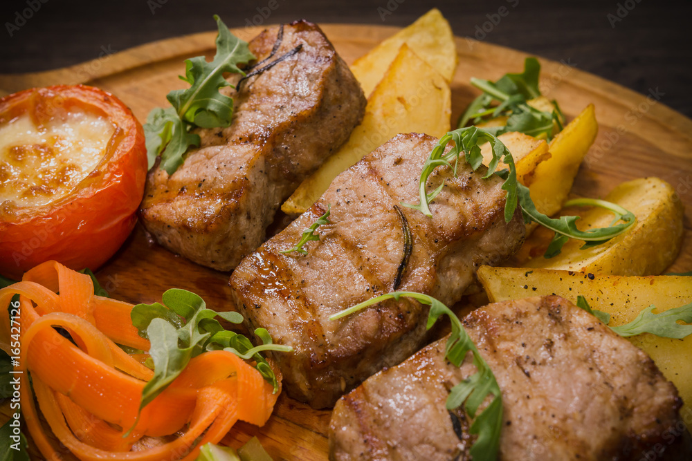Three pork steaks with fried potatoes and vegetables on a wooden background Three pork steaks with fried potatoes and vegetables on a wooden background