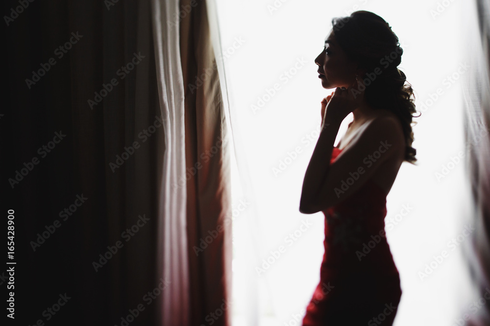 Bride puts on an earring standing before a window Bride puts on an earring standing before a window