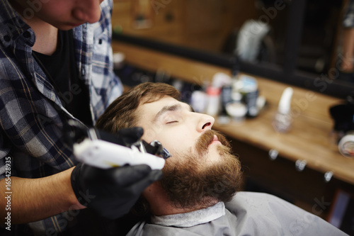 Young bearded man having his beard cut with special machine