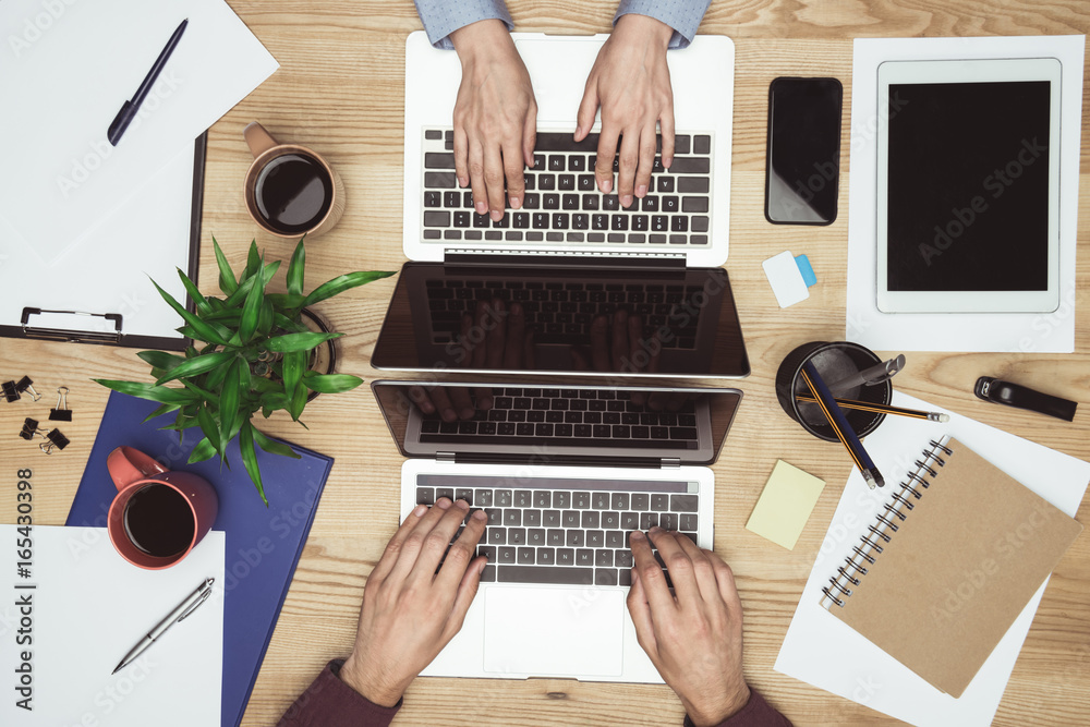 Fototapeta premium widok z góry przedsiębiorców pracujących i pisania na laptopach w miejscu pracy z gadżetami i materiałami biurowymi