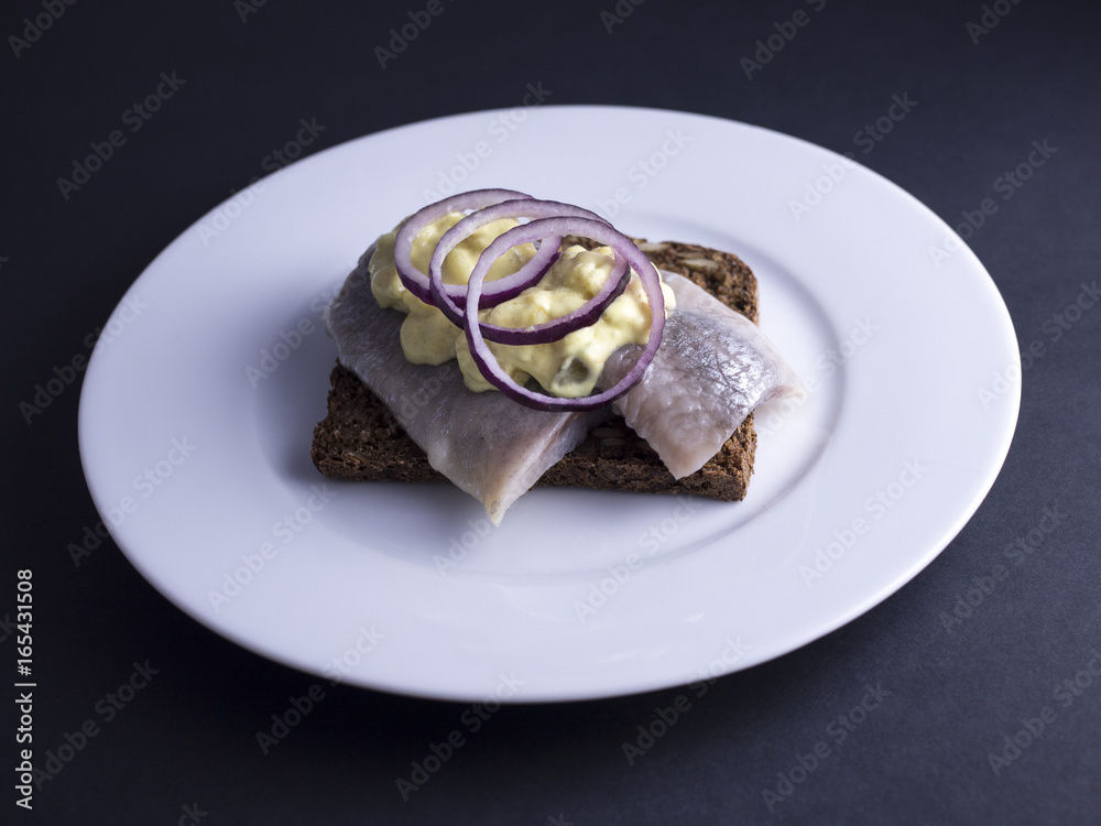 Traditional Danish open faced sandwich (smoerrebroed) with marinated herring, curry sauce and raw onion rings