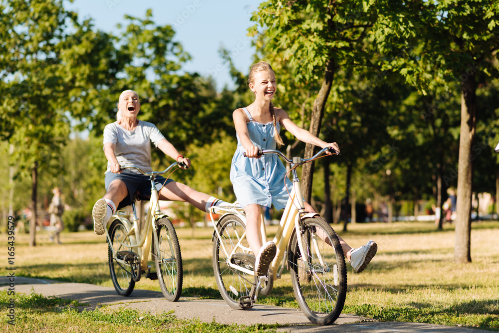 Overjoyed teenager girl and her granddaughter riding bicycles Overjoyed teenager girl and her granddaughter riding bicycles