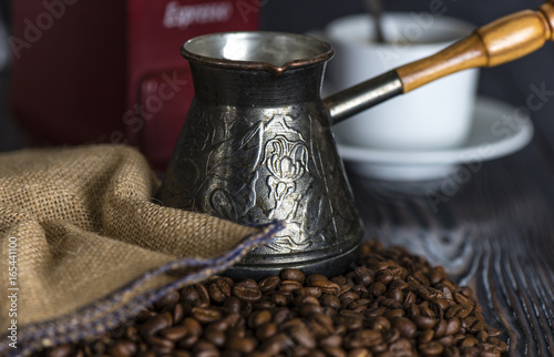 Grains of coffee next to a bag and a coffee grinder and turka