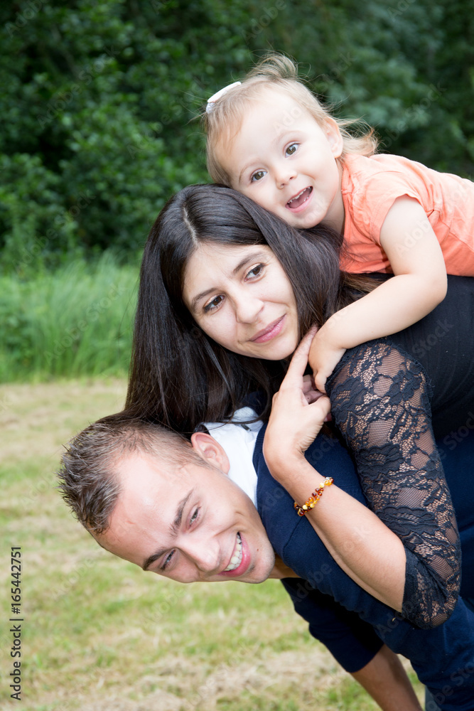 on father shoulders mother and daughter in fun in outdoors park on father shoulders mother and daughter in fun in outdoors park