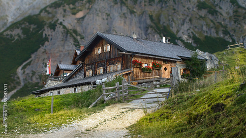 Panoramic view in the Alps with traditional mountain hut and fresh green mountain pastures on a sunny day, Austria.