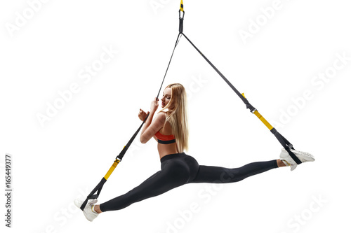 Beautiful young fitness woman in sportswear doing a split exercising with suspension straps isolated on white background