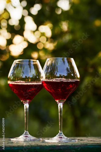 Two glasses of red wine on table in the vineyard at sunset