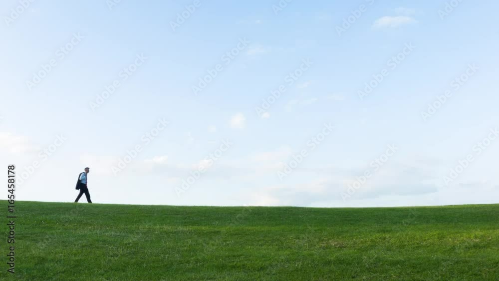 Low angle view of a Solitary middle aged Caucasian businessman walking over a hill themes of getting away from it all solitude endings Low angle view of a Solitary middle aged Caucasian businessman walking over a hill themes of getting away from it all solitude endings