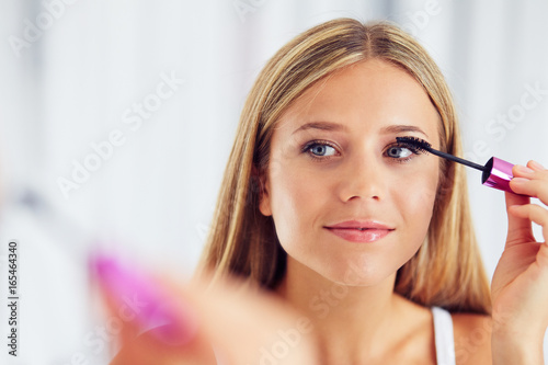 Beauty portrait of woman applying makeup and looking in the mirror. Painting eyelashes with mascara