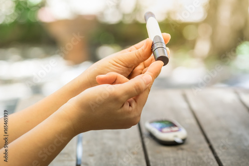 Close up of woman hands using lancet on finger to check blood sugar level by Glucose meter using as Medicine, diabetes, glycemia, health care and people concept. photo