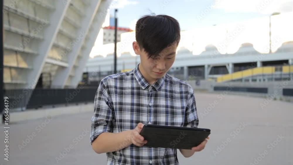 Asian man in city using tablet computer PC outdoors wearing checkerboard shirt. Asian man in city using tablet computer PC outdoors wearing checkerboard shirt.