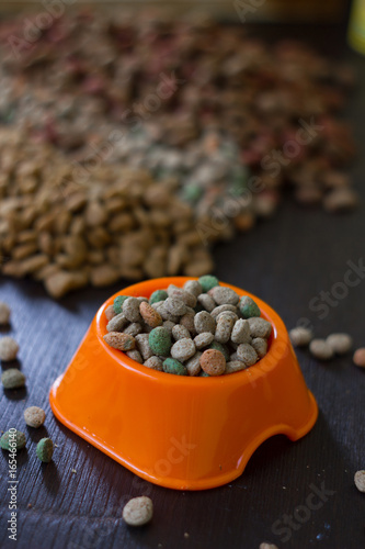 Plastic bowl with dry pet food on black wooden board.