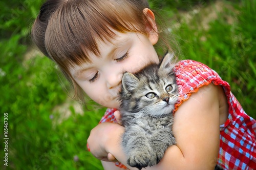 outdoor portrait of a cute little girl with small kitten, girl playing with cat on natural background