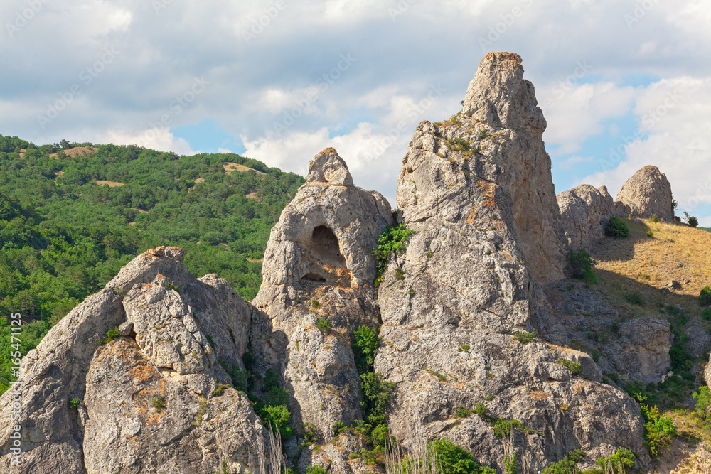 The mountain is an unusual form with a grotto in the background of hills with forests and a cloudy sky. Delikli-Kaya rock, peninsula of Crimea
