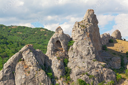 Vászonkép The mountain is an unusual form with a grotto in the background of hills with forests and a cloudy sky