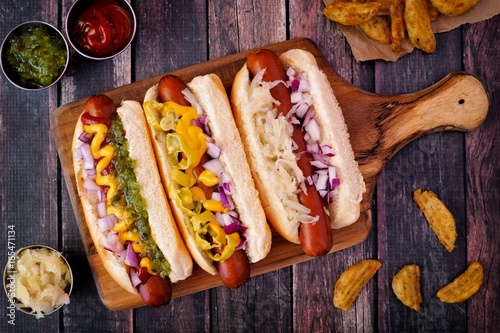 Hot dogs fully loaded with assorted toppings on a paddle board, overhead scene