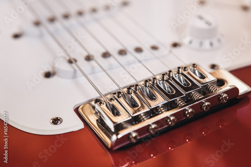 Part of modern electric six string guitar red color with glossy finish, pickups and control knobs isolated on wooden background close up view photo