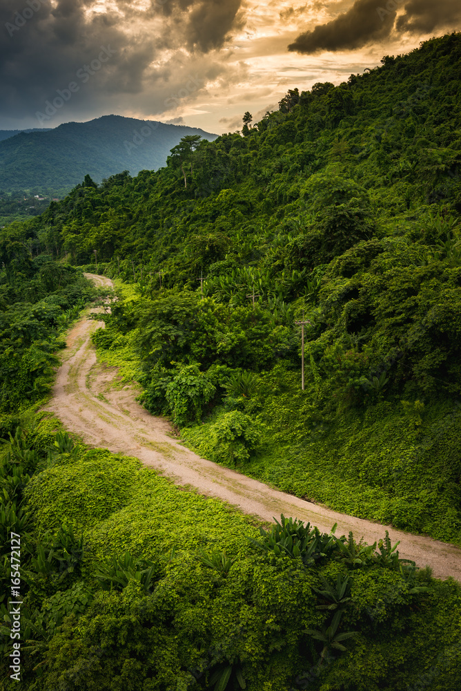 Landscape of dirt rugged countryside road and two mountains with 2 colored blue and orange cloudy sky