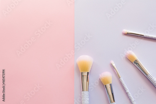 Five makeup brushes with lettering on the handle on pink and purple background. Have copy space.
