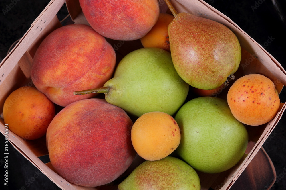 Pears, peaches and apricots in a basket on a dark background