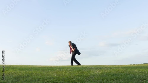 Happy carefree middle aged Caucasian businessman playing air guitar on a hill messing about daydreaming being a rock musician