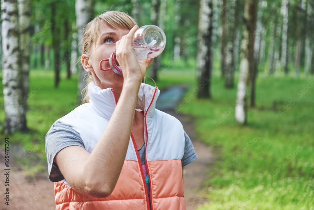 Young girl drinking water with a bottle in a park.
