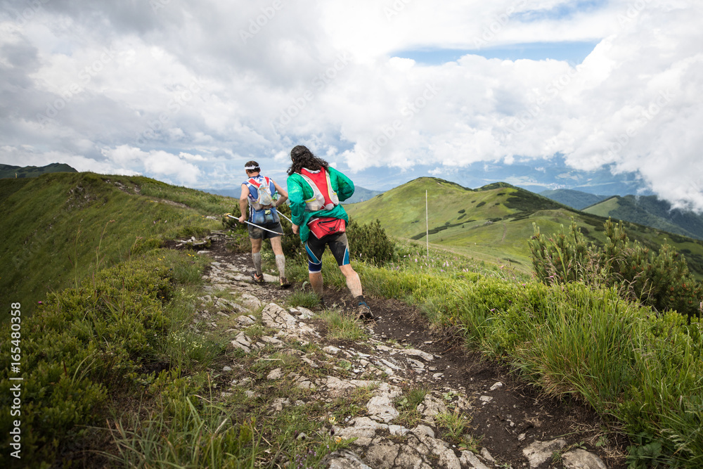 two runners running together on high mountain adventure trail with epic scenery view