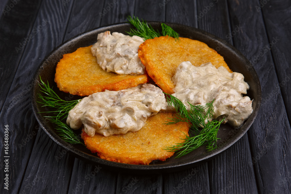 Potato flapjacks (draniki) with onion and mushroom creamy sauce in cast-iron pan Potato flapjacks (draniki) with onion and mushroom creamy sauce in cast-iron pan