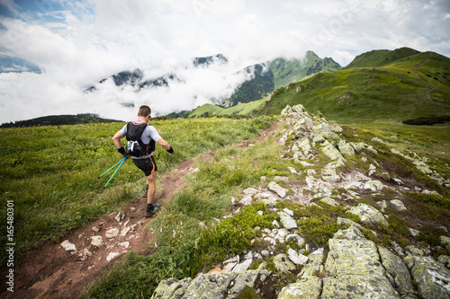 middle age male runner with backpack and poles on the mountain trail after rain with cloudy view