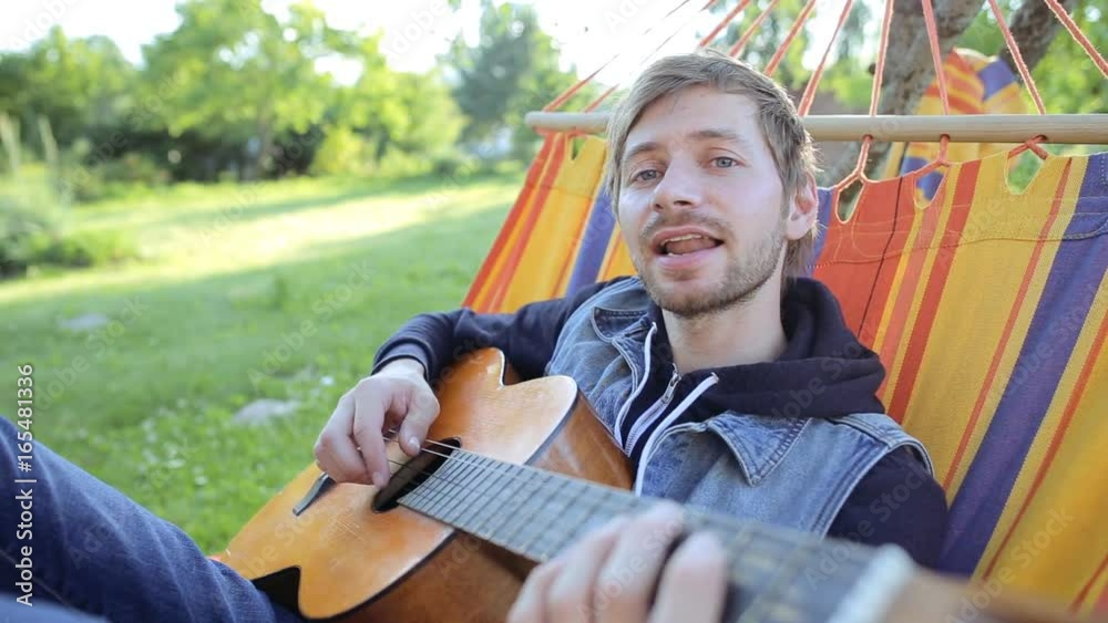 Young hipster man playing acoustic guitar in a hammock on a summer day