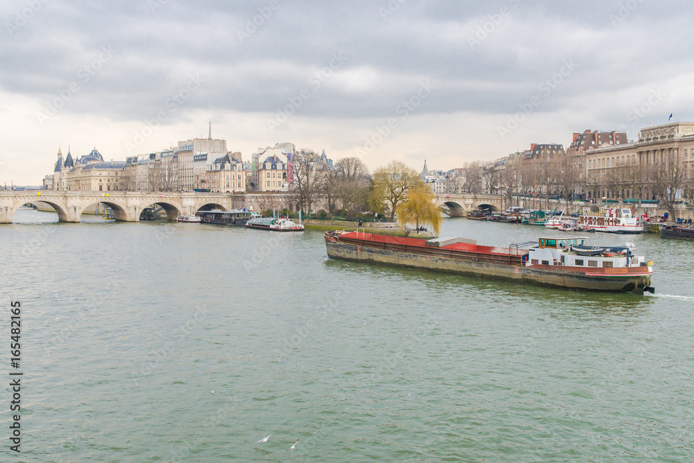 Obraz premium Paris, view of the Seine from the pont des Arts, with the Pont-Neuf and a barge crossing 